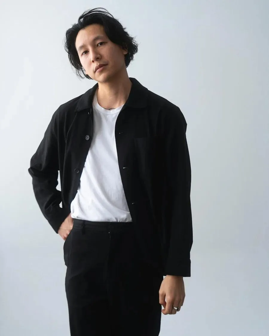 A man in a black jacket and pants stands poised for a Tinder profile photo