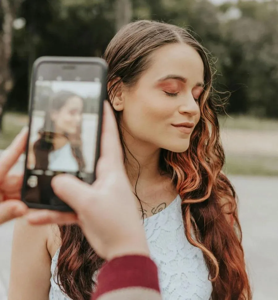 A woman smiling while taking a selfie with her phone, perfect for her Tinder profile picture.