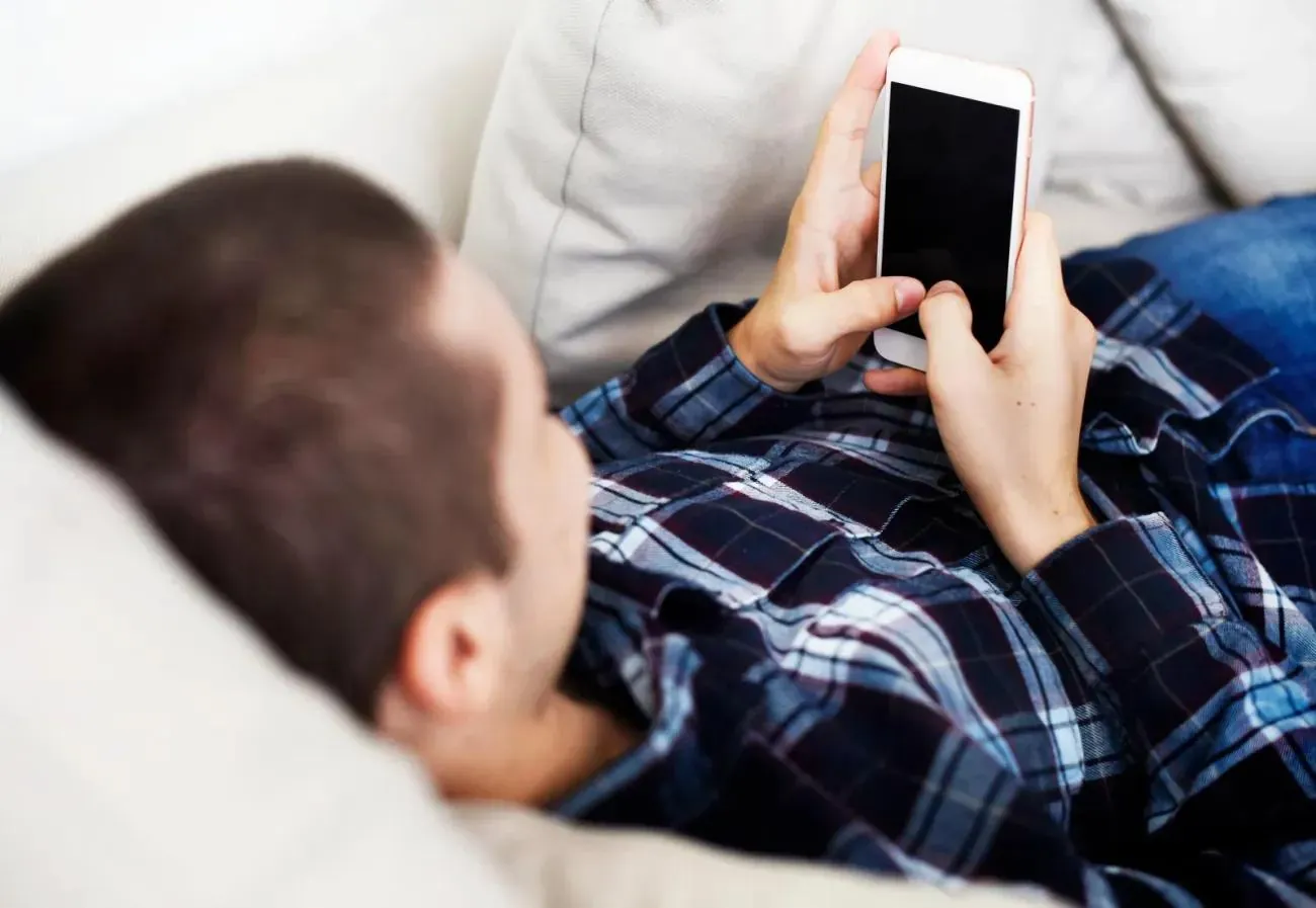 Man laid on couch using smartphone. Source: © <a href='https://www.123rf.com/profile_rawpixel'>rawpixel</a>, <a href='https://www.123rf.com/free-images/'>123RF Free Images</a>
