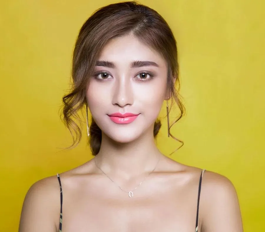 An attractive Asian woman with pink lips stands in front of a bright yellow background, perfect for a Tinder profile image.