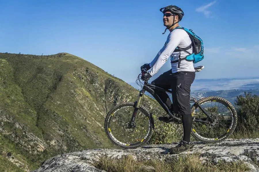 A man stands on a mountain top with his bike, showcasing adventure and outdoor spirit for his Tinder profile.